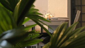 Una mesa de comedor con varias copas de vino y una vela, rodeada de plantas verdes.