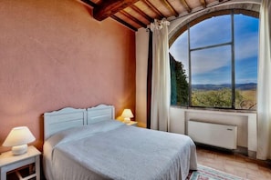 A bedroom with a bed, nightstands, a window with a view of the countryside, and a radiator. - Country House Nazzano in Vineyards/ near San Gimignano Florence Siena - Ro (Gambassi Terme)