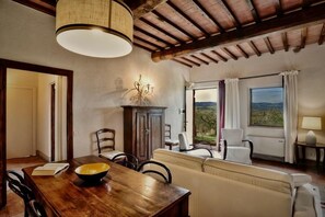 A dining area with a wooden table, chairs, and a bowl. There is a sofa and a window with curtains. - Country House Nazzano in Vineyards/ near San Gimignano Florence Siena - Ro (Gambassi Terme)