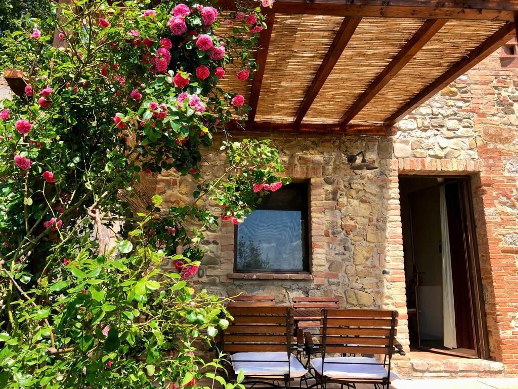 A stone building with a wooden pergola, a window, and a bench area.