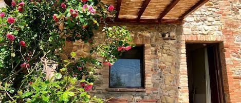 A stone building with a wooden pergola, a window, and a bench area.