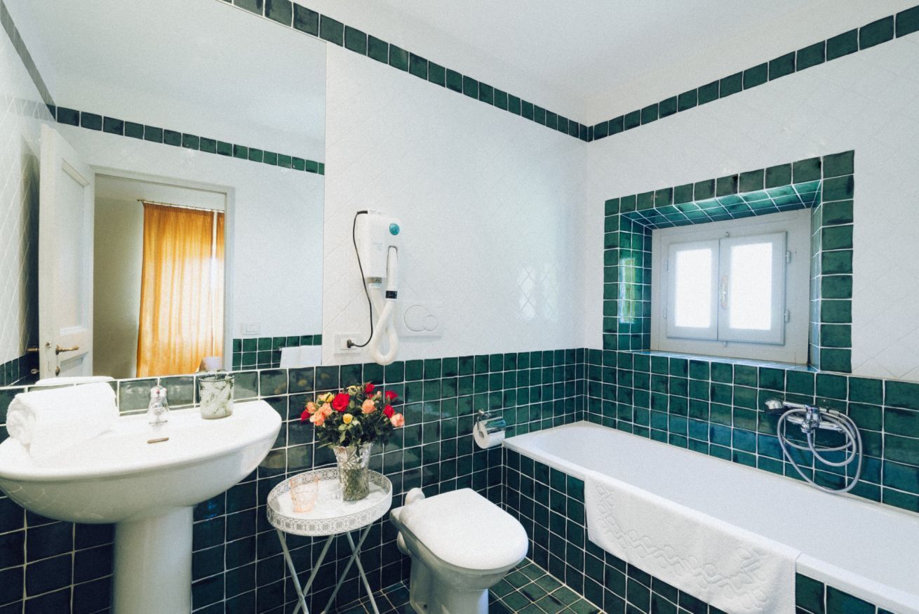 Een badkamer met een wit wastafel, toilet en bad. Er is een raam boven het bad en een handdoek hangt aan de muur.