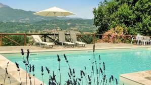 A swimming pool with a view of mountains, surrounded by lounge chairs and an umbrella.