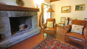 A cozy living room with a stone fireplace, leather armchairs, a patterned rug, and framed artwork on the walls.