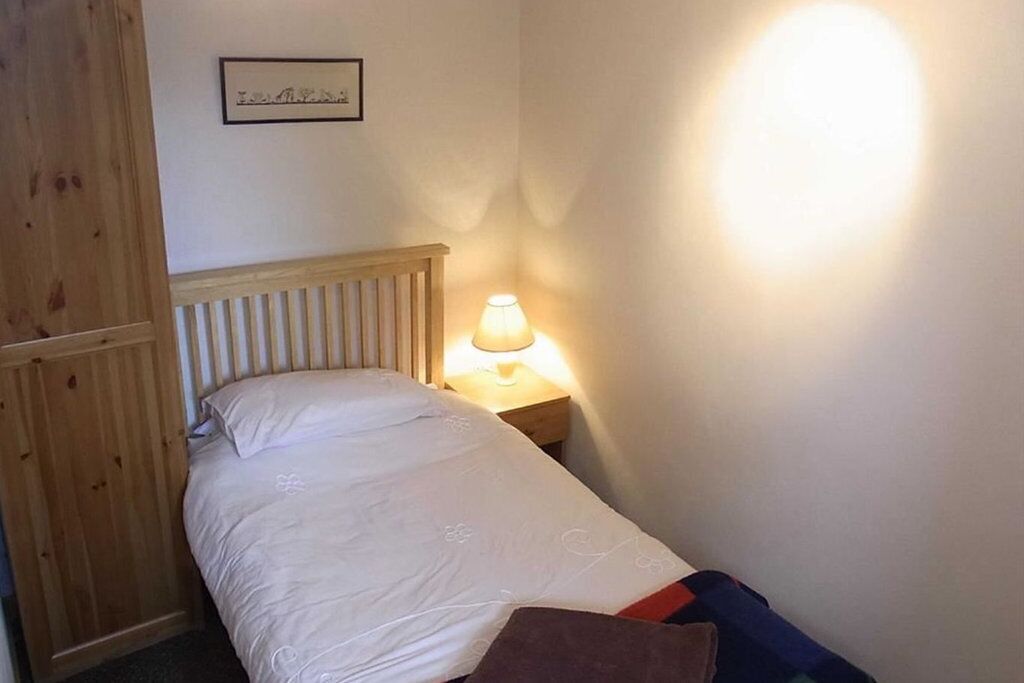 Un lit simple avec une tête de lit en bois, une lampe de chevet et un tableau encadré au mur.