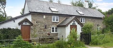 A stone cottage with a sloped roof, two chimneys, and a small porch.