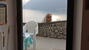 A room with a view of a lake and mountains, a white chair, a potted plant, and a tiled floor. - Two-room apartment in Residence with swimming pool and panoramic lake view in Sale Marasino (Sale Marasino)