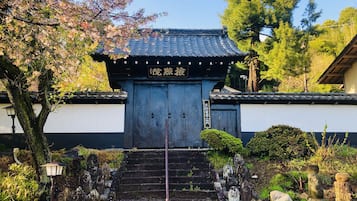 Un tradicional torii japonés con una escalera de madera que conduce hasta él, rodeado de faroles de piedra y un jardín bien cuidado.