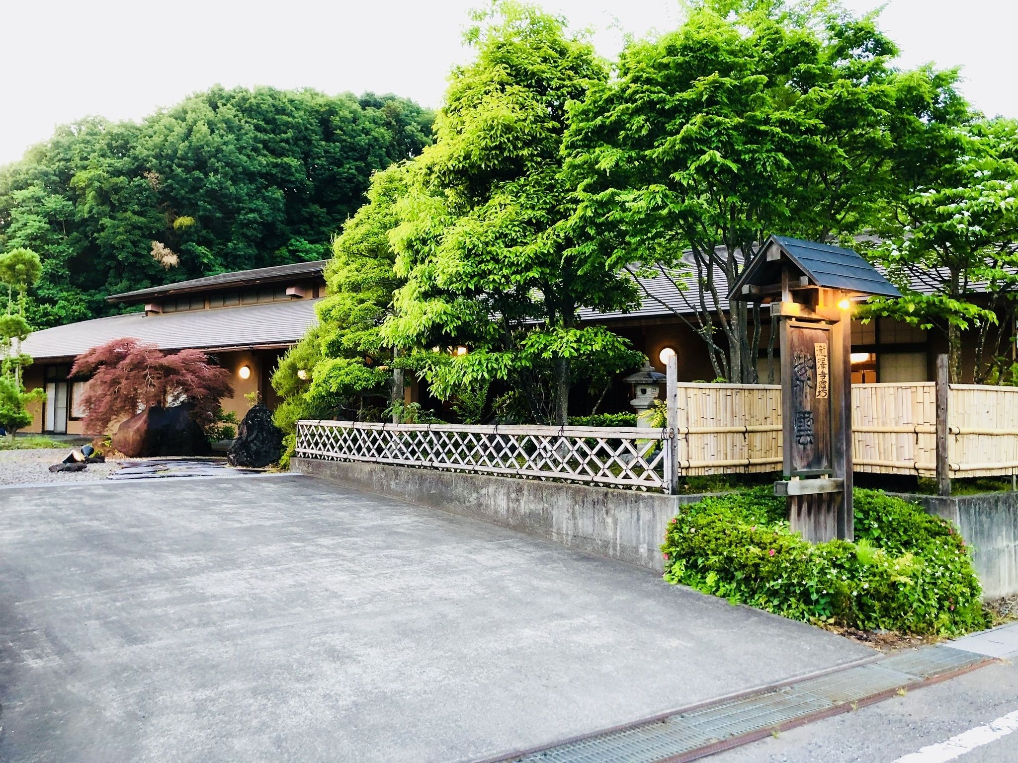 A traditional Japanese building with a wooden fence, a stone lantern, and lush greenery.
