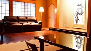 A modern living room with a leather sofa, a glass coffee table, and a traditional Japanese artwork. - Ryutakuzenji (Takasaki)