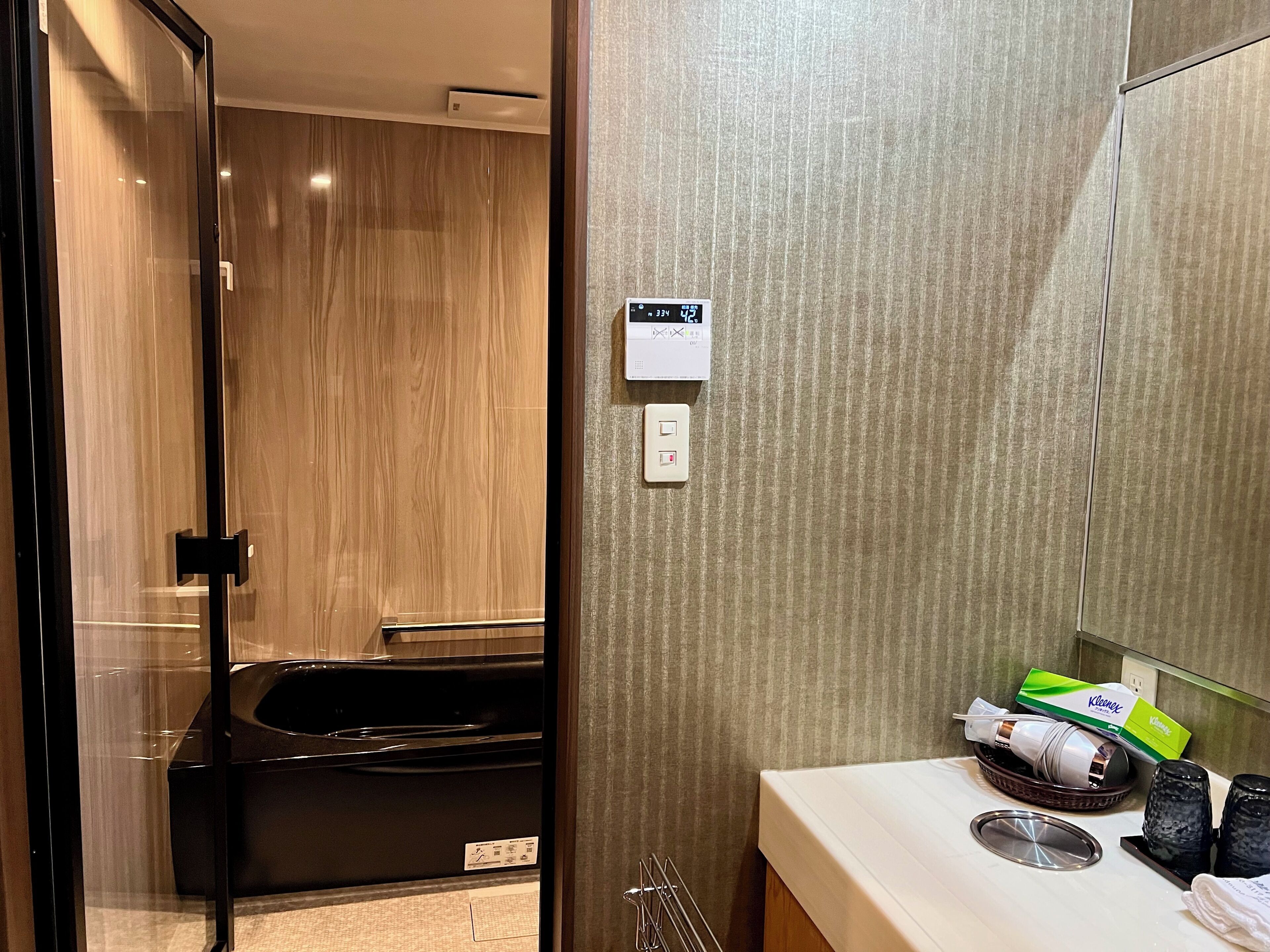 Un baño moderno con cabina de ducha de vidrio, una bañera negra, un tocador con espejo y un perchero para toallas.
