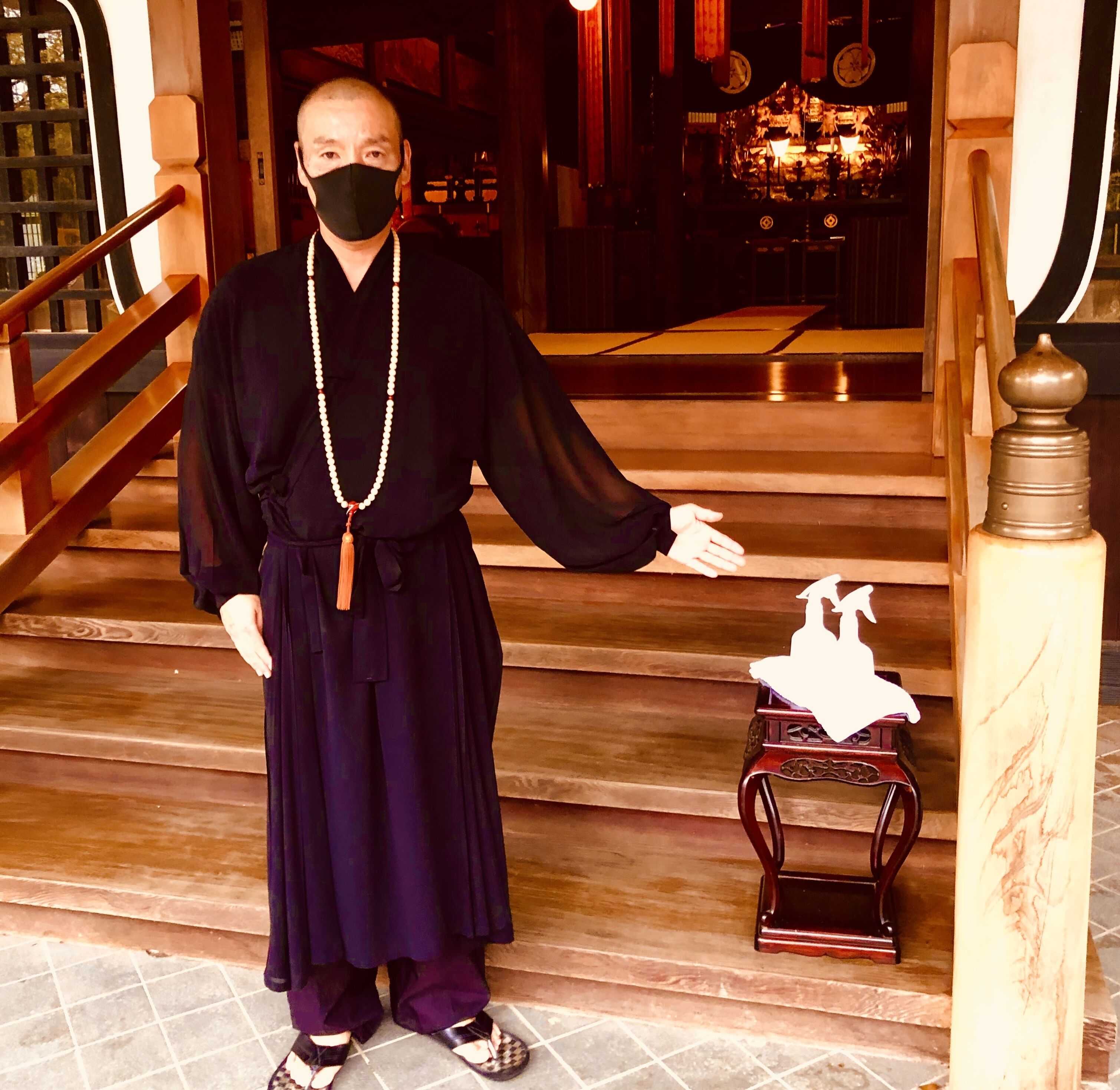 A person in traditional attire standing on a staircase with a small table and a statue.
