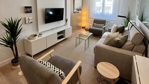 Ein modernes Wohnzimmer mit Flachbildfernseher, grauem Sofa, Couchtisch aus Holz und einem kleinen Beistelltisch.