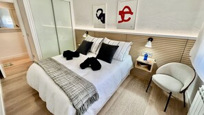 Ein modernes Hotelzimmer mit einem großen Bett, einem Nachttisch mit Lampe, einem Sessel und einem Bild an der Wand.
