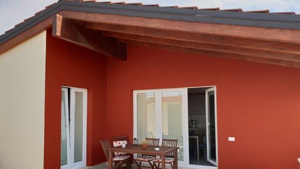 A red building with a covered patio, a table with chairs, and a sliding glass door leading to an interior space. - Sea view Penthouse sea view (Quartu Sant'Elena)