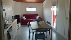 A compact living space with a kitchenette, a red sofa, a dining table with chairs, and a TV. - Sea view Penthouse sea view (Quartu Sant'Elena)