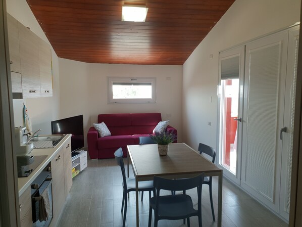 Un espace de vie compact comprenant un coin cuisine, un canapé rouge, une table  à manger avec des chaises et un téléviseur.