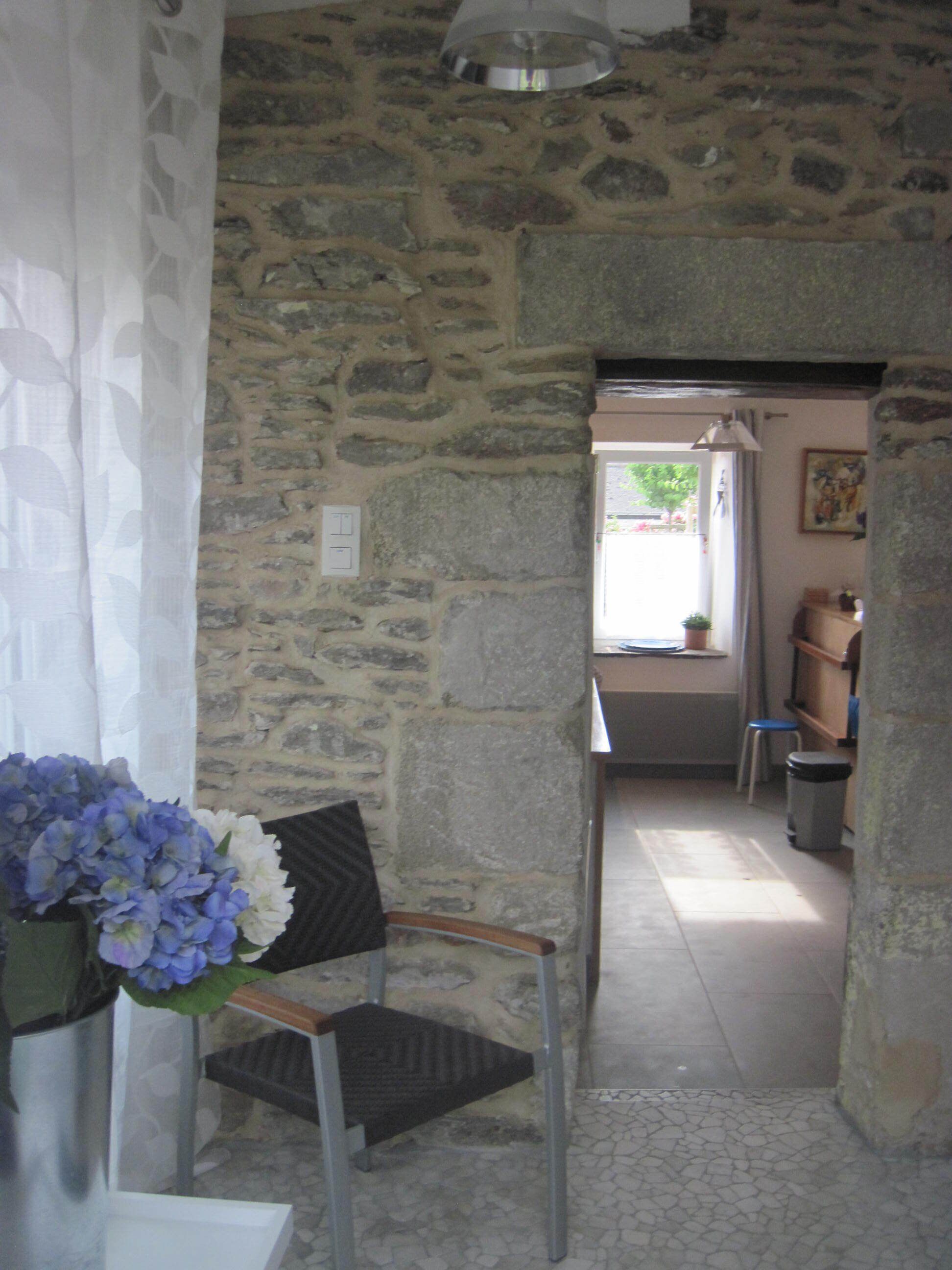 A stone-walled room with a chair, a small table, and a window with a view of greenery outside.