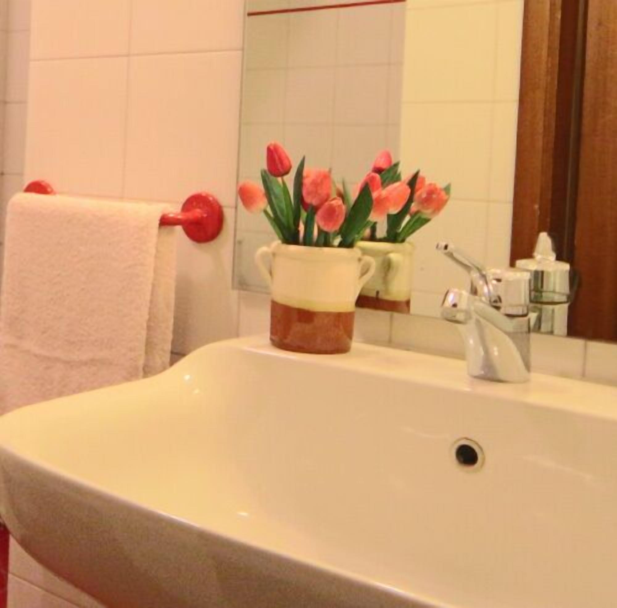 A bathroom with a white sink, a mirror, and a vase with pink flowers.