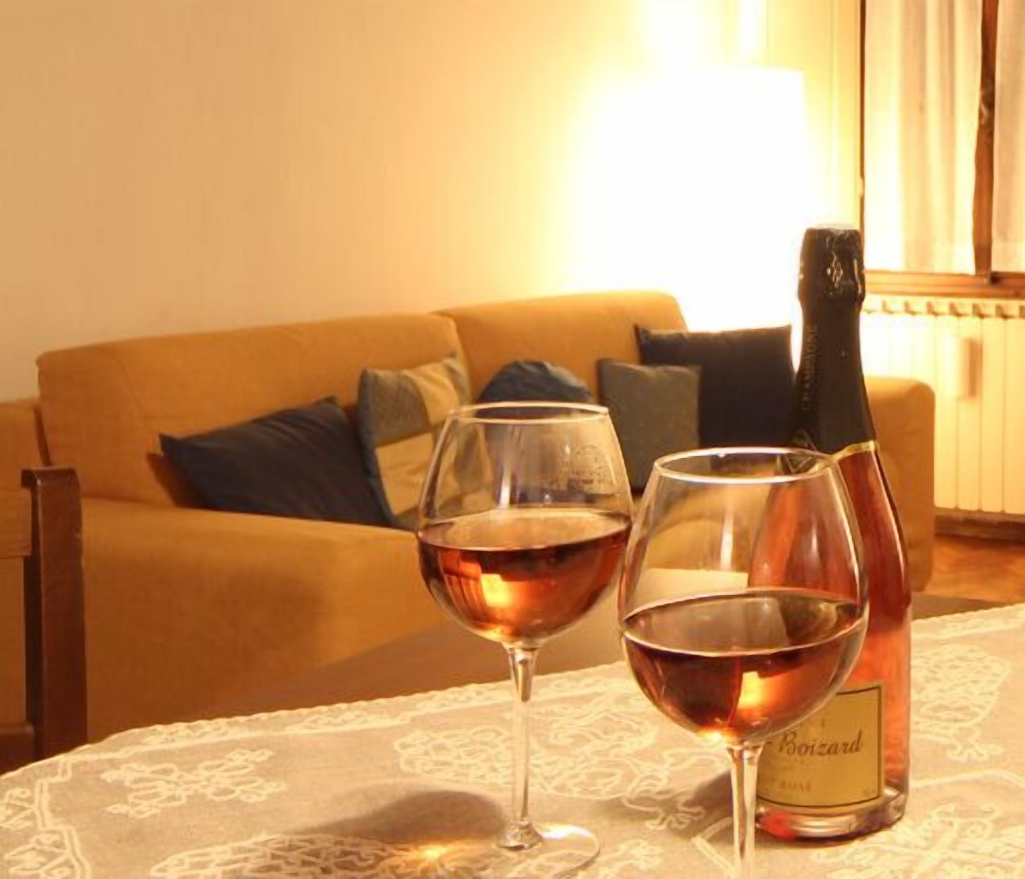 A room with a sofa, two wine glasses, and a bottle of wine on a table.