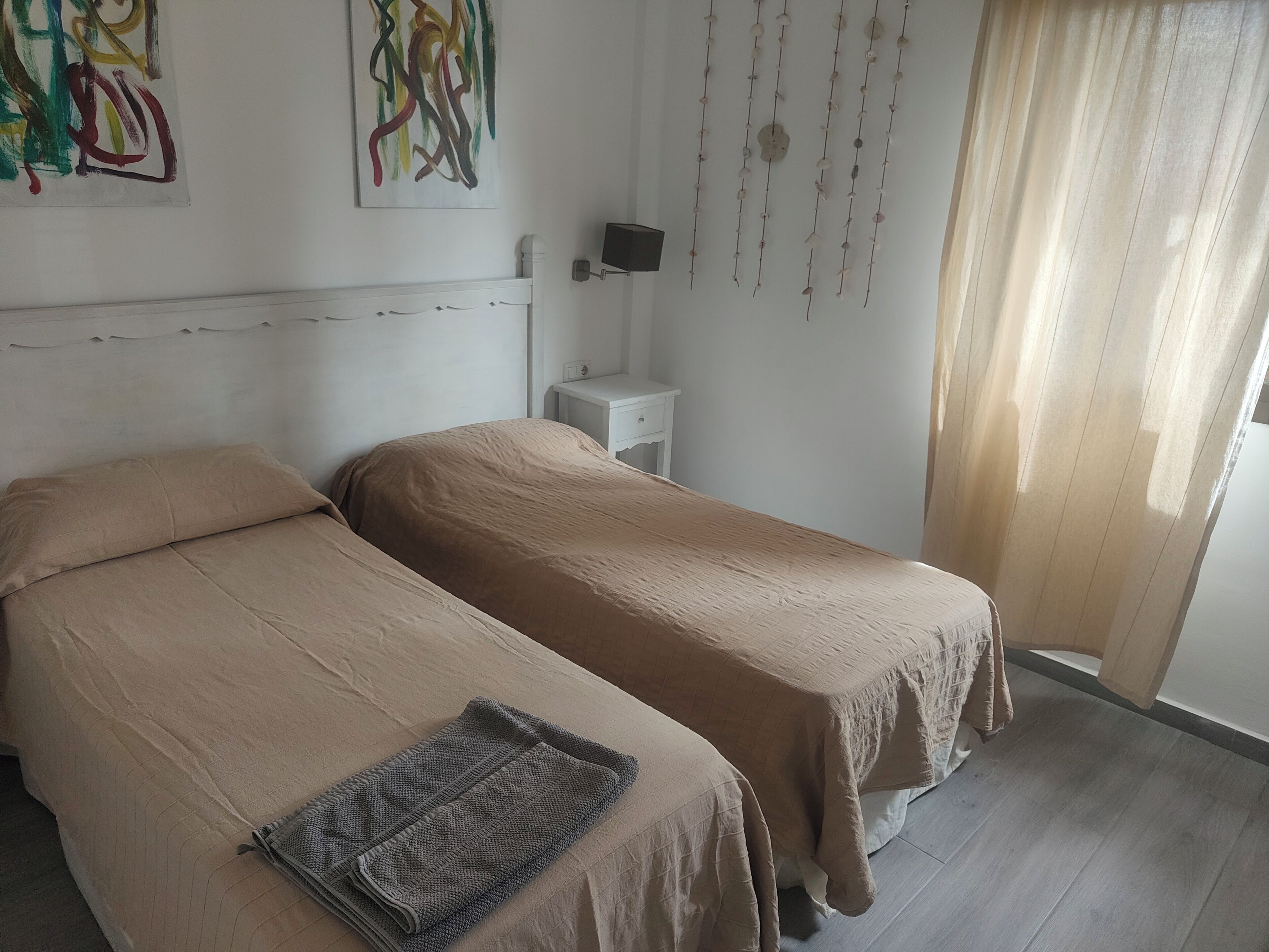 Une chambre avec deux lits, une petite table de chevet, un téléviseur fixé au mur et un rideau.