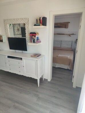 A bedroom with a TV, a white dresser, a bed, and a closet.