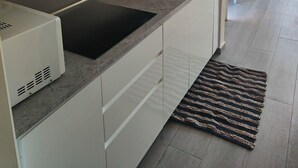A modern kitchen with white cabinets, a black induction cooktop, a stainless steel sink, and a patterned rug on the floor. - Apartment/ flat - Corralejo (Corralejo)