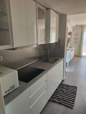 Moderni keittiö, jossa on valkoiset kaapit, musta induktioliesi, ruostumattomasta teräksestä valmistettu pesuallas ja kuviollinen matto lattialla.