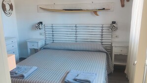 A bedroom with a striped bedspread, two bedside tables, a wall-mounted shelf, and a life preserver decoration. - Apartment/ flat - Corralejo (Corralejo)