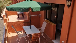 A patio with a table and chairs, a green umbrella, and a view of the building's exterior. - Apartment/ flat - Corralejo (Corralejo)