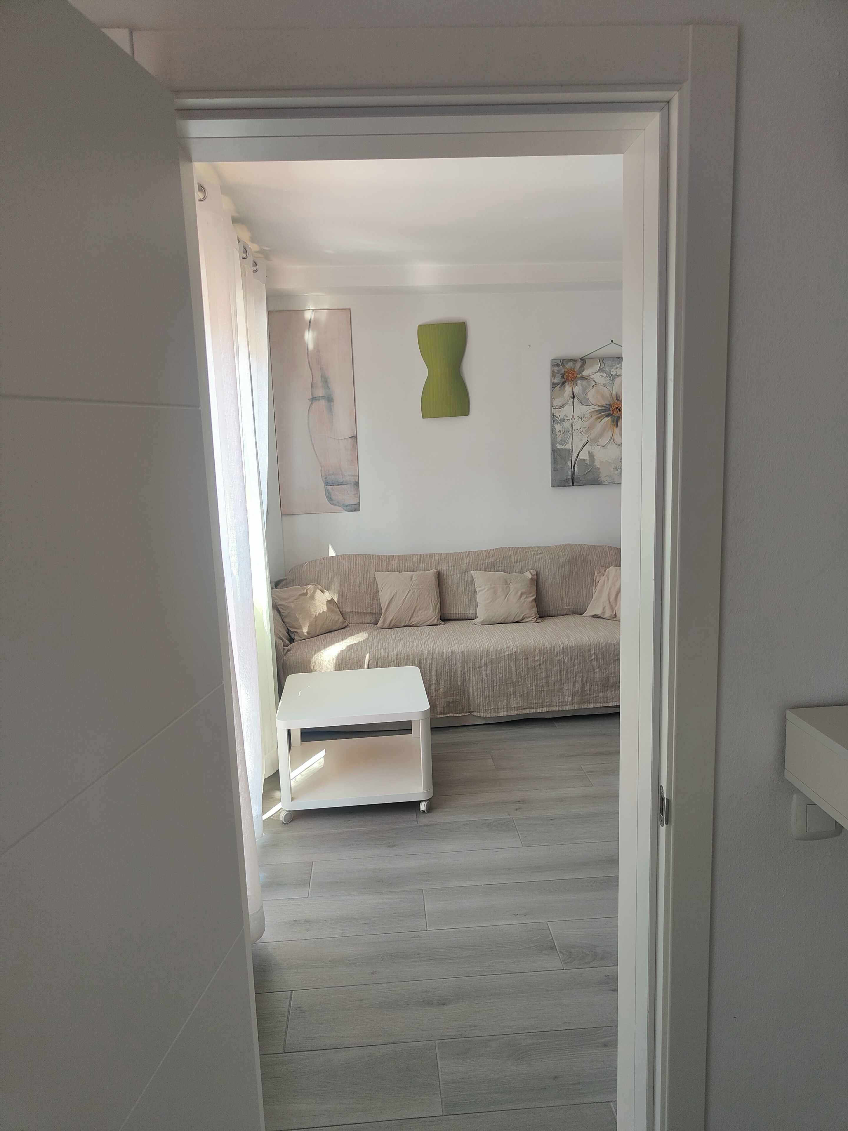 Een interieur van een kamer met een bank, een witte bijzettafel en een schilderij aan de muur.