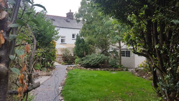 A garden pathway leading to a white house with a grey roof, surrounded by lush greenery and a well-maintained lawn. - Family House with garden in Lake District National Park - sleeps 8 (Bootle)