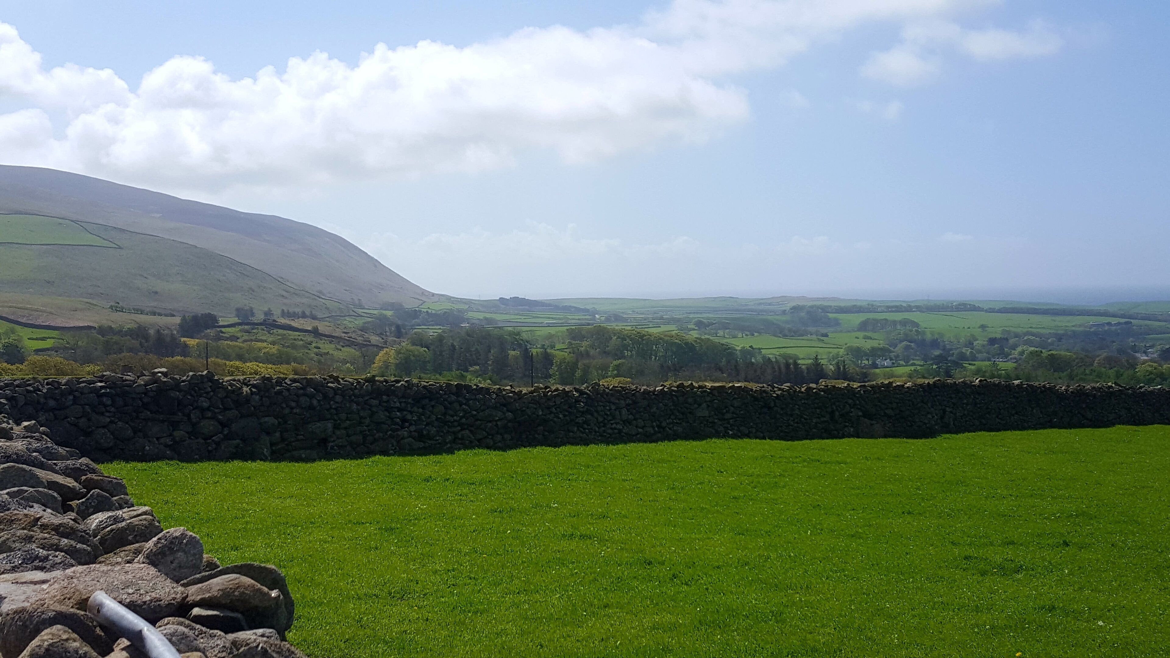A stone wall and a grassy field with a distant hill.