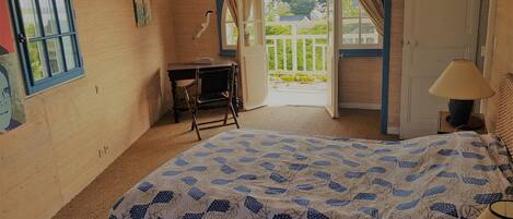 Ein Schlafzimmer mit Bett, Schreibtisch, Stuhl, Lampe und Blick ins Freie.
