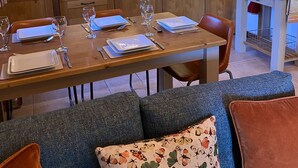 A dining area with a wooden table set for four, a kitchen with white cabinets and a tiled backsplash, and a seating area with a sofa and cushions. -  Homely ground floor 2 bedroom apartment with stunning views  (Samoëns)