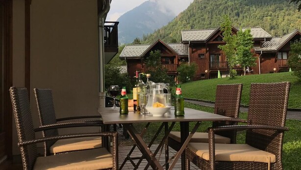 A wooden table with wicker chairs on a patio overlooking a mountain. -  Homely ground floor 2 bedroom apartment with stunning views  (Samoëns)