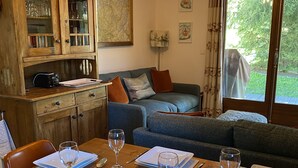 A cozy living room with a dining table set for four, a wooden cabinet with glass doors, and a large window with curtains. -  Homely ground floor 2 bedroom apartment with stunning views  (Samoëns)