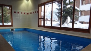An indoor swimming pool with clear blue water, large windows, and a view of a snowy landscape. -  Homely ground floor 2 bedroom apartment with stunning views  (Samoëns)
