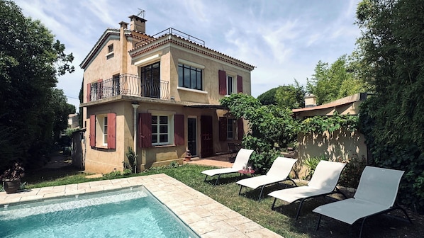 A two-story house with a swimming pool, outdoor seating, and a garden.