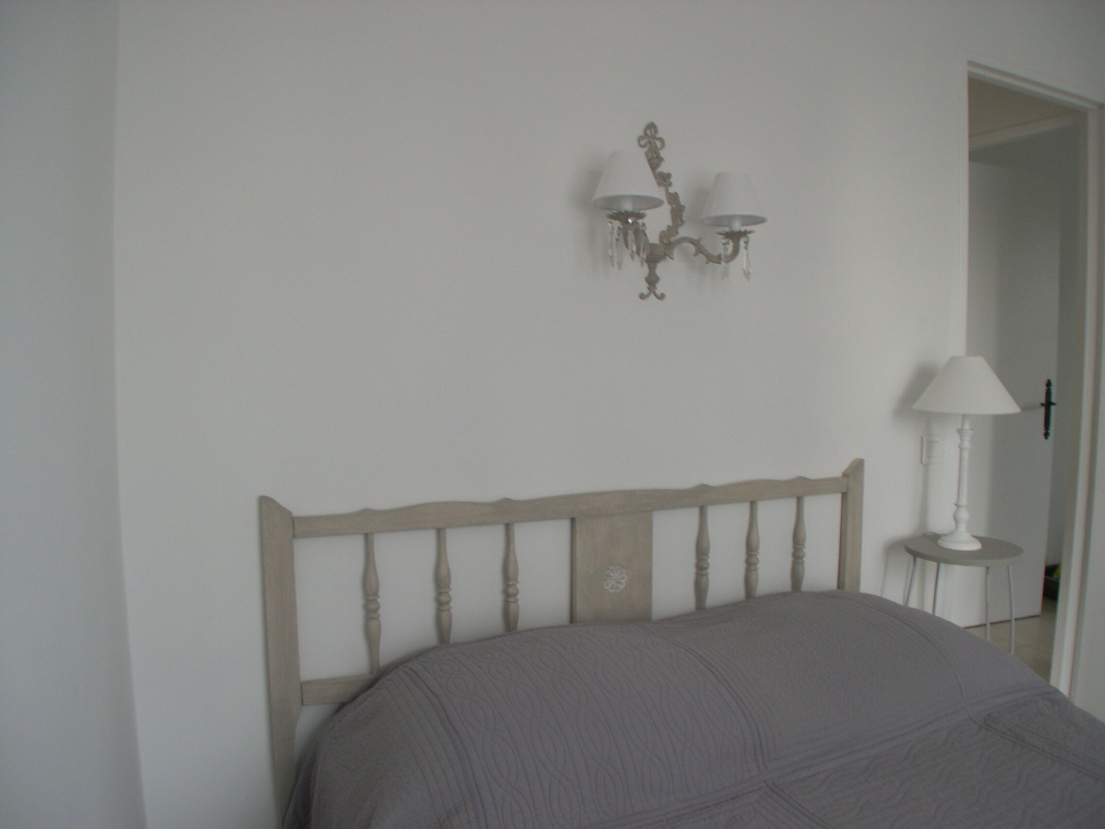 A bedroom with a wooden headboard, a bedside table with a lamp, and a wall-mounted light fixture.