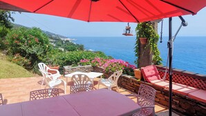 An outdoor patio with a table and chairs, a red umbrella, and a view of the sea. - Beautiful house on the sea 300 m from the beach (Brando)