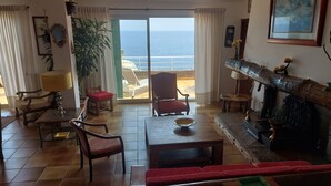 A living room with a view of the sea, a fireplace, and a dining area with a table and chairs. - Beautiful house on the sea 300 m from the beach (Brando)