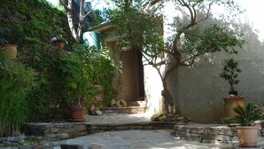 A stone pathway leading to a rustic building with a door, surrounded by potted plants and a large rock. - Beautiful house on the sea 300 m from the beach (Brando)