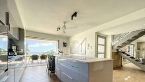 Una cocina moderna con una isla grande, un comedor con sillas y vistas al océano.