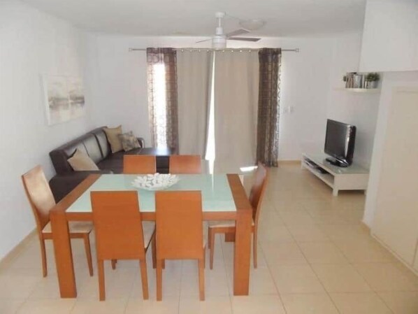 A dining area with a table and chairs, a sofa, a television, and curtains.