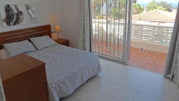 Een hotelkamer met een bed, nachtkastje, lamp, een schuifglazen deur naar een balkon en uitzicht.