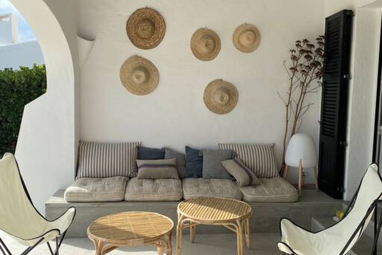 A modern outdoor seating area with a sofa, two round wicker tables, and a wall-mounted decorative item.