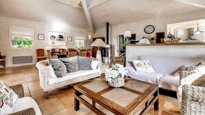 A spacious living room with high ceilings, wicker furniture, a wooden coffee table, and a large chandelier. - Charming villa with heated swimming pool between pool and ocean at Cap Ferret (Lège-Cap-Ferret)