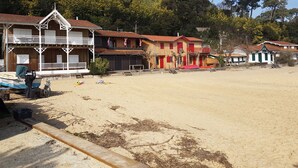 A beachfront property with multiple wooden buildings, a boat docked outside, and a sandy beach area. - Charming villa with heated swimming pool between pool and ocean at Cap Ferret (Lège-Cap-Ferret)