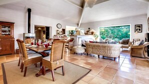A spacious living area with a high ceiling, wicker furniture, and a large window offering a view of greenery. - Charming villa with heated swimming pool between pool and ocean at Cap Ferret (Lège-Cap-Ferret)